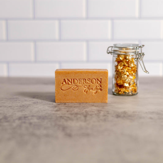 natural bar soap with gold shimmer and a glass jar of gold flakes on a grey countertop