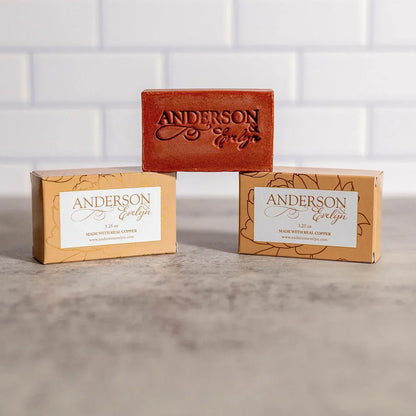 All-natural copper soap bar and boxes on gray countertop with white tile background