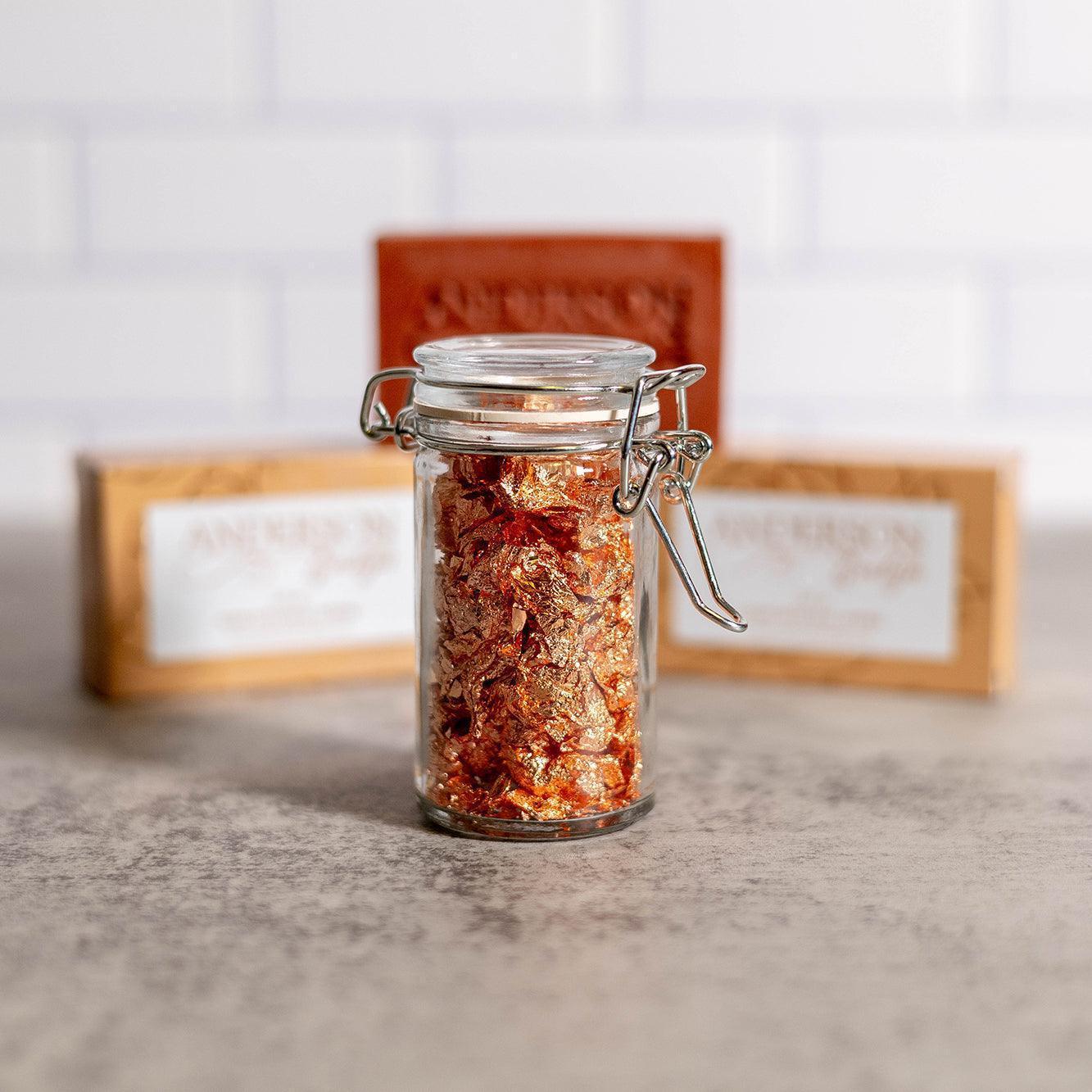 Glass jar filled with gold and copper foil flakes, natural soap bars in background