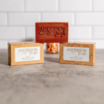 Natural copper soap bar and packaging on countertop with white tile background