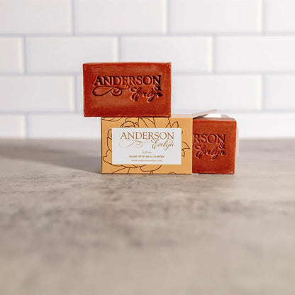 Natural copper-infused soap bars with embossed logo on a counter, tile background.