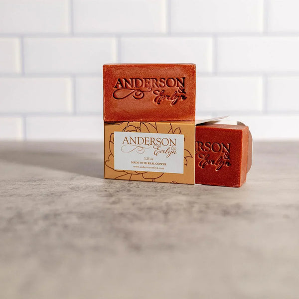 Natural copper soap bars stacked on a marble counter, embossed and boxed, in bright kitchen setting.