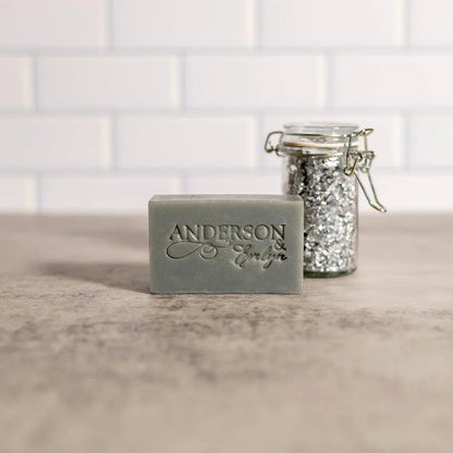 Gray natural soap bar with embossed text beside a glass jar of metallic flakes on countertop