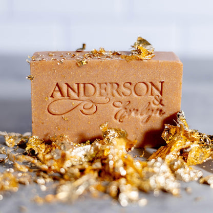 All-natural soap bar with etched lettering, surrounded by gold and silver leaf pieces on a countertop.