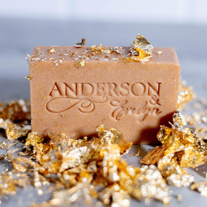 All-natural soap bar with engraved text, surrounded by gold and metallic flakes