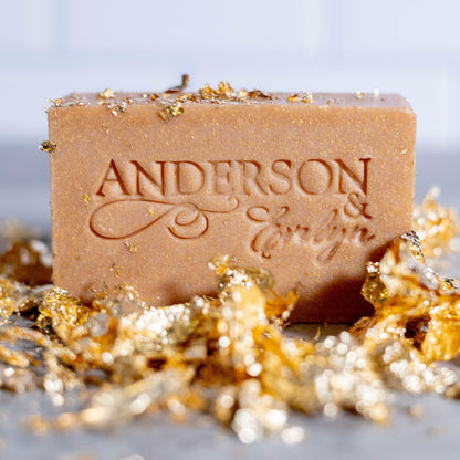 Natural bar soap with embossed logo, surrounded by gold leaf accents on a countertop