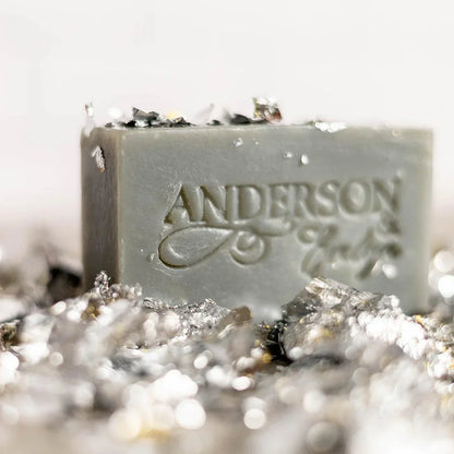 Natural gray soap bar with embossed text, surrounded by metallic mineral flakes