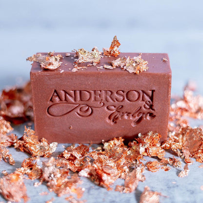 Natural soap bar with metallic leaf flakes on marble surface, engraved with product name.