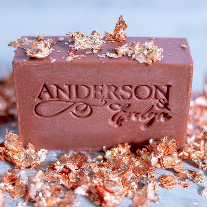 Brown natural soap bar with embossed text, surrounded by gold and copper foil accents