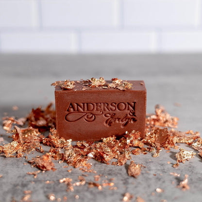 Copper-infused natural soap bar with metallic leaf flakes on gray surface
