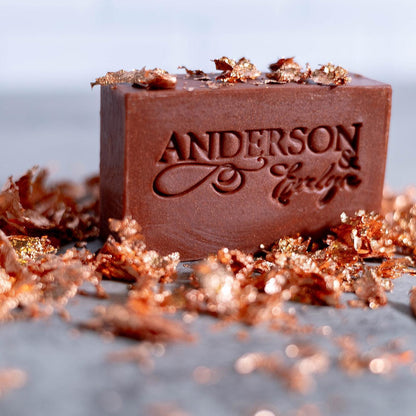 Brown natural soap bar with copper, gold flecks, engraved logo, on stone surface