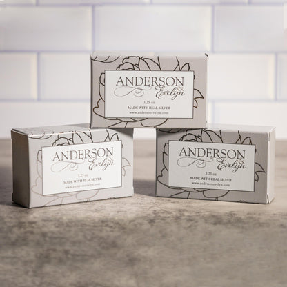 Three boxes of silver-infused all-natural soap on a stone surface with floral design.