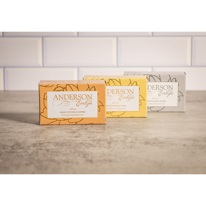 Three bars of all-natural soap with copper, gold, and silver ions on a bathroom counter.