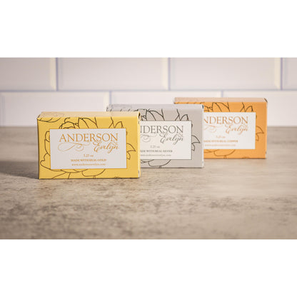Three bars of natural soap with gold, silver, and copper ions on a stone surface.