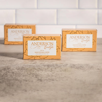 Natural soap bars with copper on a countertop, floral packaging, bathroom setting