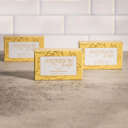 Three yellow boxes of natural gold-infused soap on a stone countertop