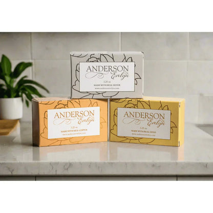 Three boxes of natural soap infused with copper, silver, and gold on a bathroom counter.
